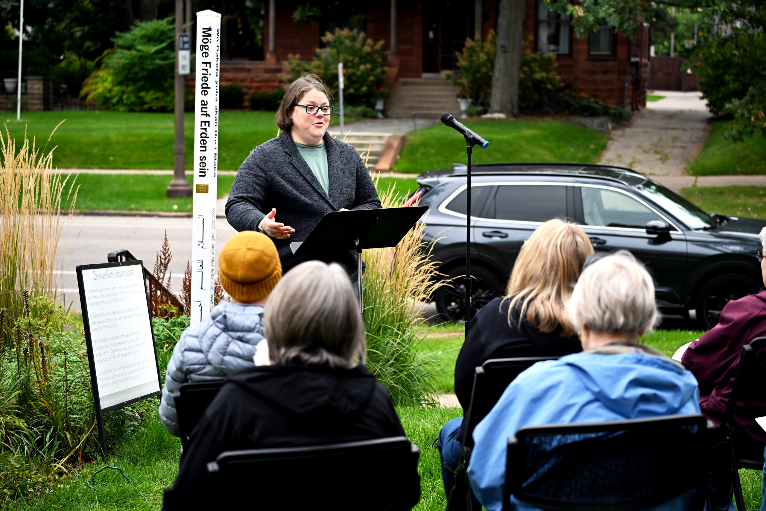 Elsa Kendig speaks at the House of Hope Peace Pole commissioning, with the Peace Pole behind her.