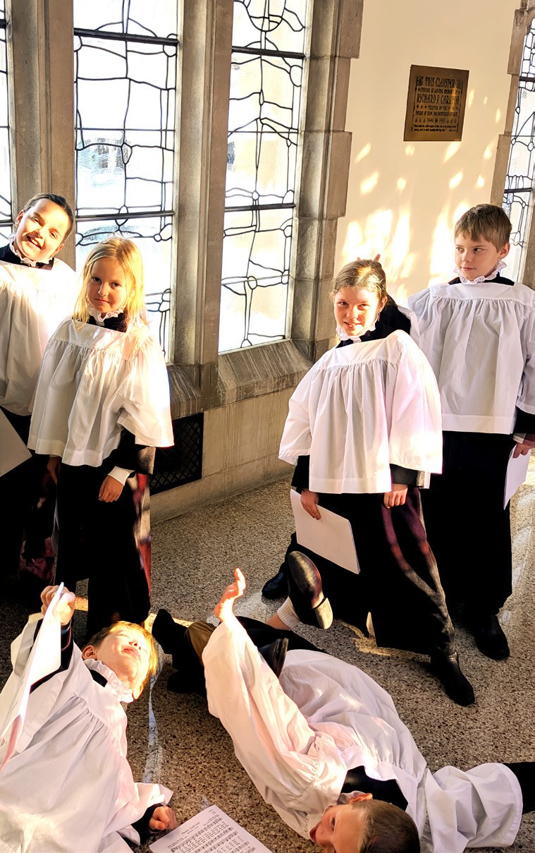 Children in choir robes gather beside the church’s stained-glass windows.
