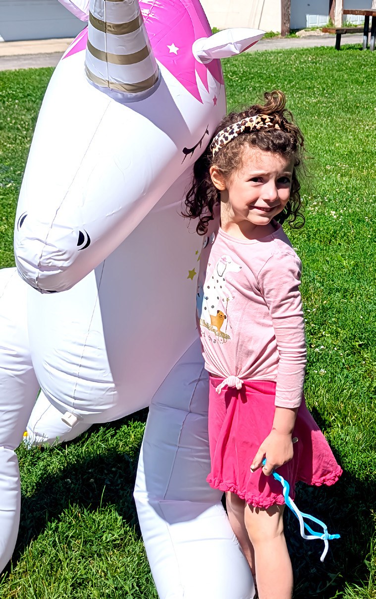 A child stands beside a large inflatable unicorn on the church lawn.