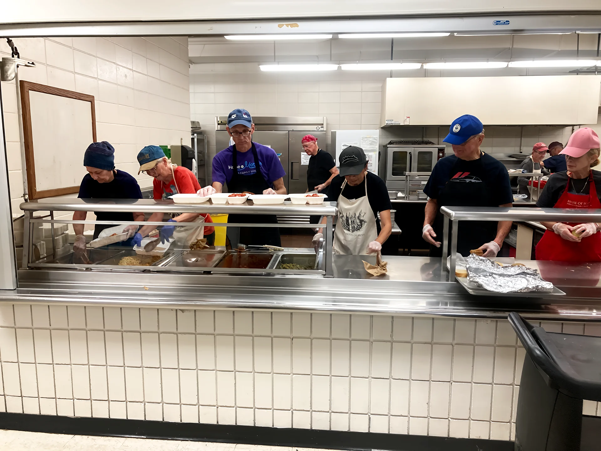 Volunteers serving meals across the kitchen counter.